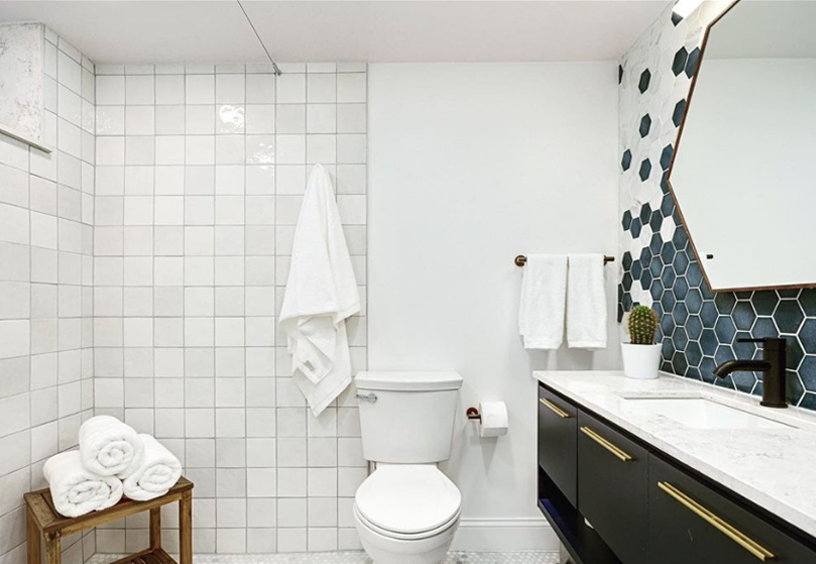 White square shower tile and hexagonal blue and white backsplash tile adorn a remodeled basement-level bathroom. Gold hardware and white linens finish the look.